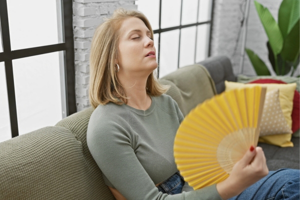 woman sitting on a sofa trying to cool down using a hand fan