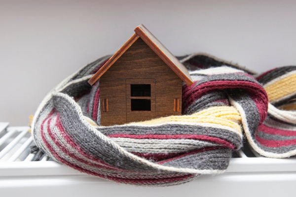 mini wooden house wrapped in a scarf on top of a home radiator depicting Reasons Heating Oil is Such a Trusted Heating Fuel